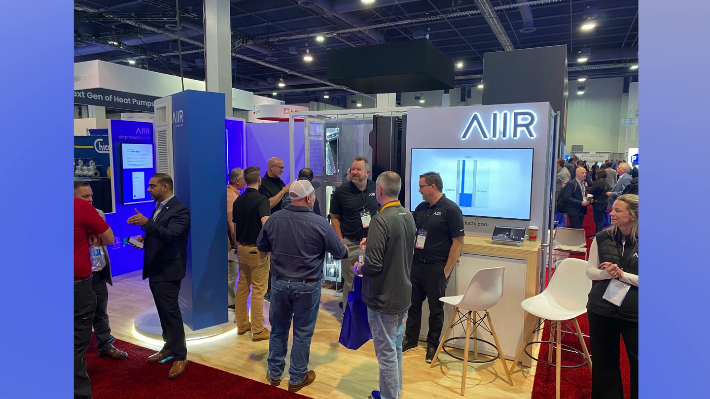 AIIR’s AHR booth in use, with a touchscreen kiosk, product displays, a large film screen, and attendees in conversation